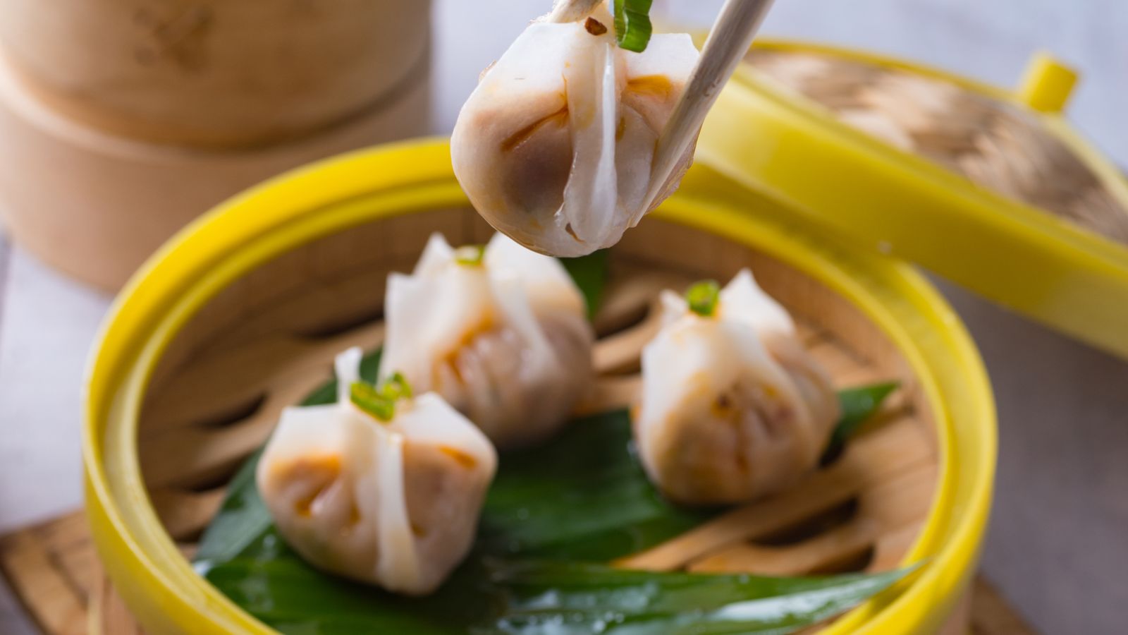 Chopsticks lifting a steamed dumpling from a bamboo steamer